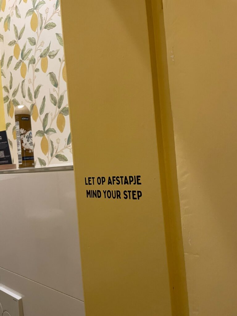 Zwarte belettering Let op afstapje en Mind your step op een gele wand