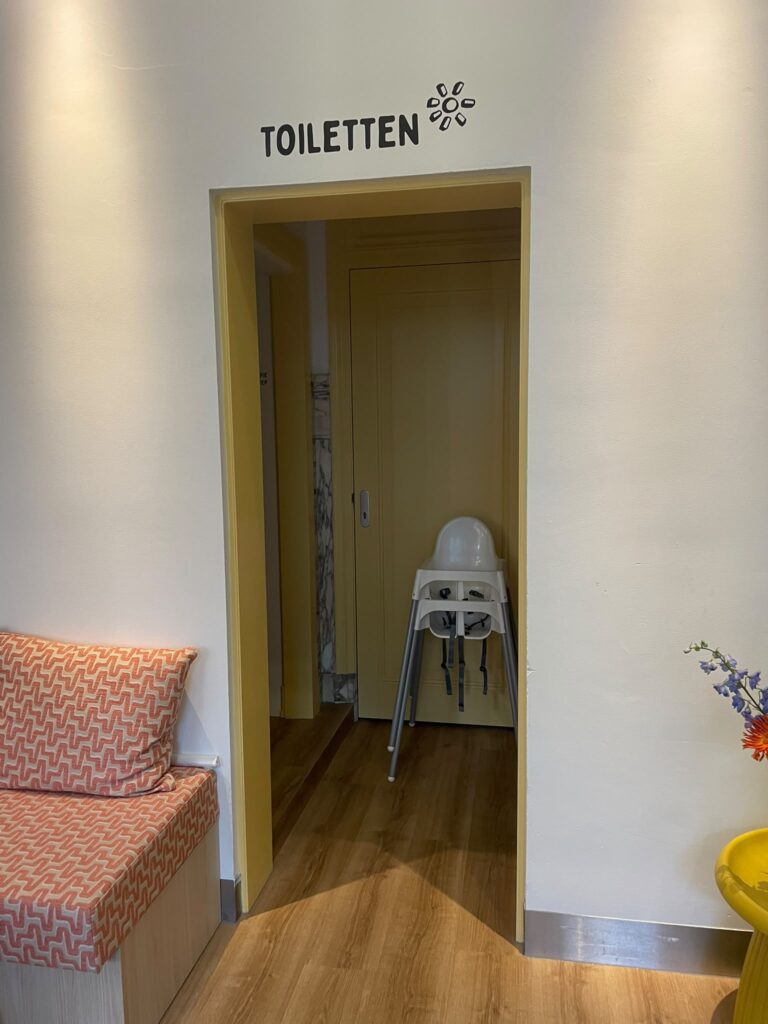 Aanduiding Toiletten met grafisch symbool boven een deuropening bij Happyness Café