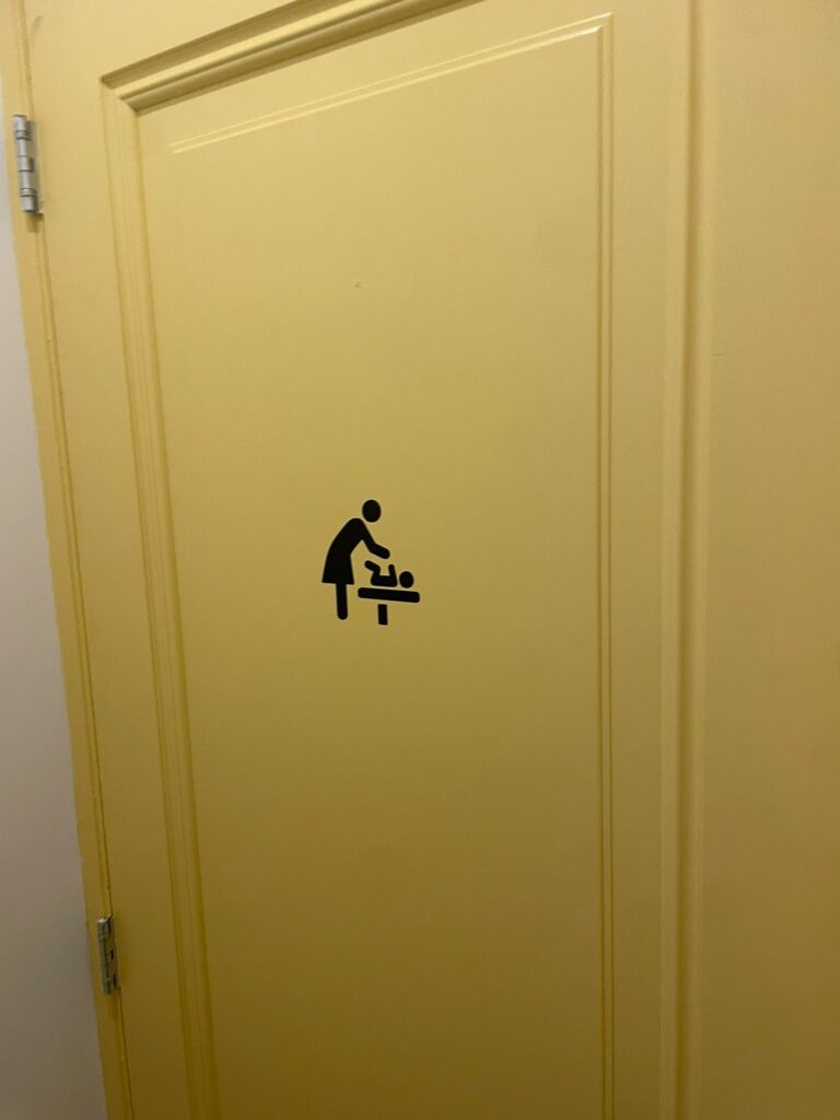 Zwart verschoonpictogram op een gele deur bij Happyness Café in Haarlem