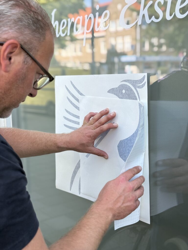 Montage van het vogelbeeldmerk op de raamfolie van Fysiotherapie Eksterlaan